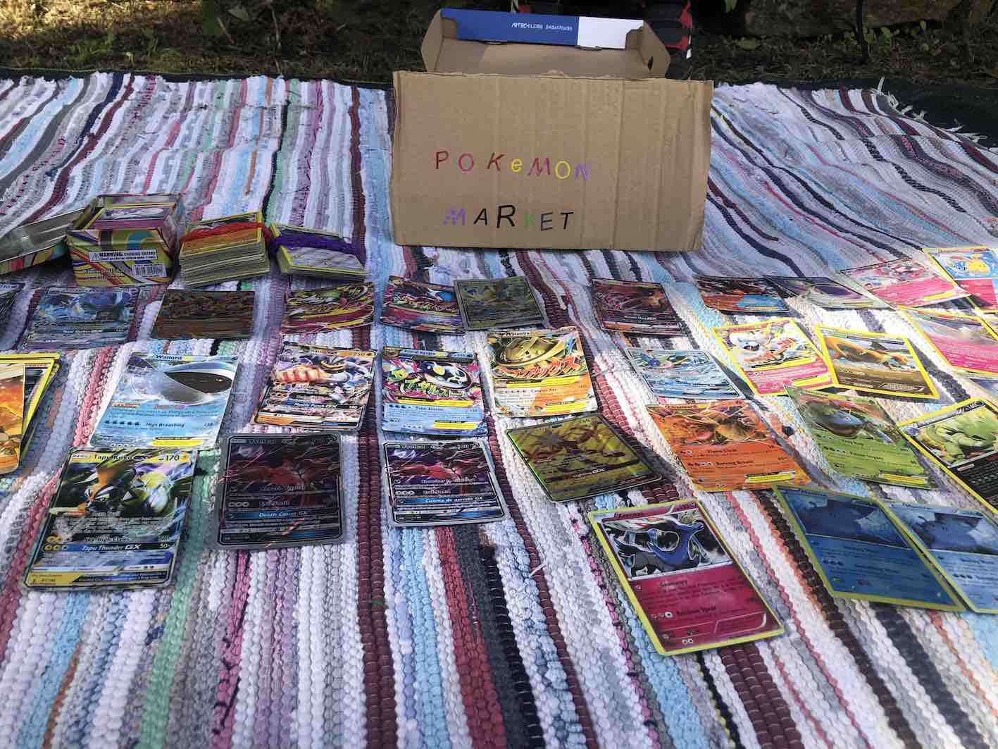 Foto de Manta com Cartas expostas e Caixa de Cartão com a Frase Colorida Pókemon Market